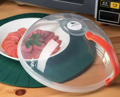 Splash guard with an orange handle covering a white plate of sliced sausage and parsley on a green woven placemat
