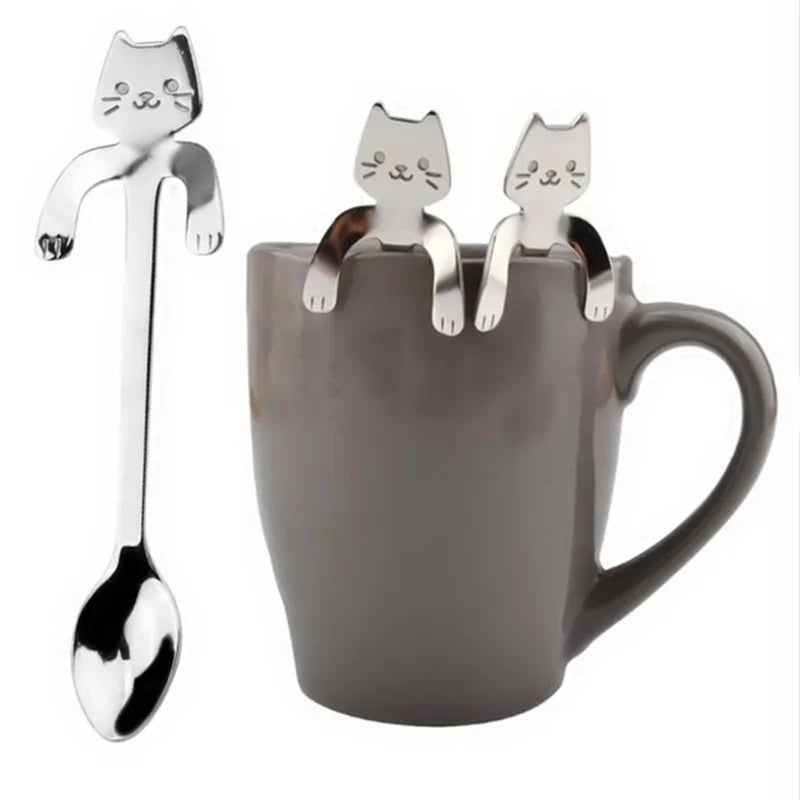 Silver cat spoon beside three matching spoons hooked onto the rim of a gray mug