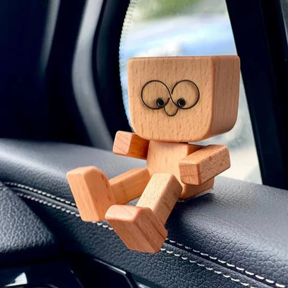 Wooden figurine seated on a car dashboard near a seatbelt, with wire-loop eyes and a small screw nose