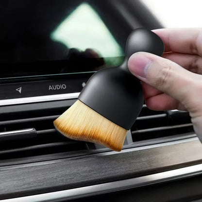 Close-up of a hand holding the brush near a dashboard air vent labeled Audio