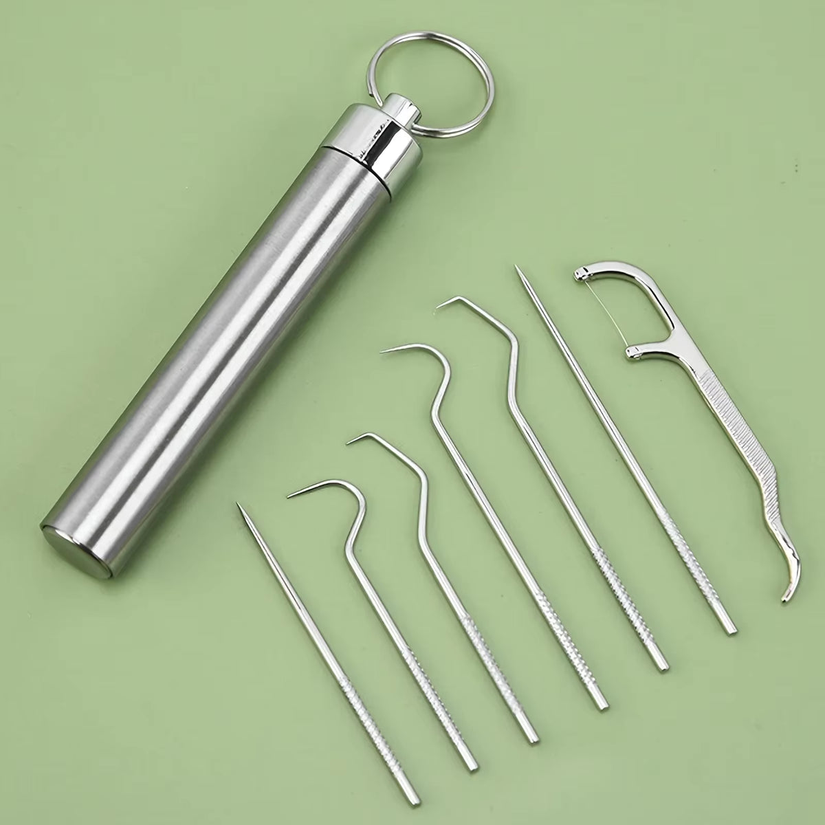 Flat lay of the toothpick canister, its cap, and seven stainless pick tools arranged on a green surface