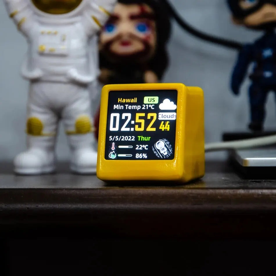 Yellow weather clock on wooden desk with astronaut and character figurines in background, showing Hawaii weather