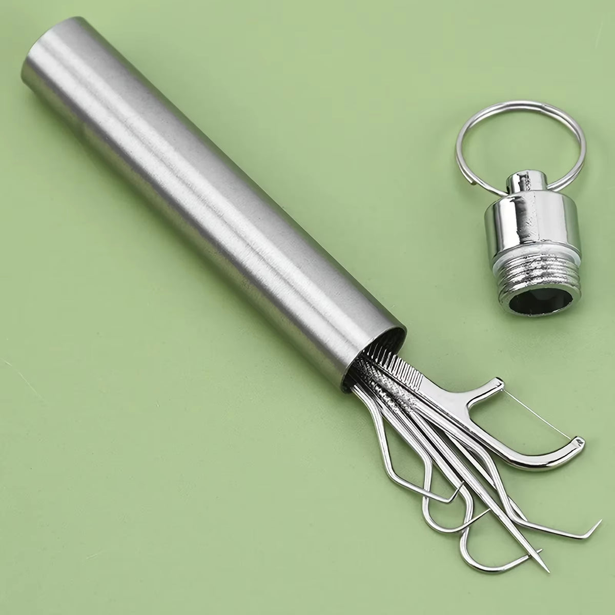 Toothpick canister with tools spilling out next to its detached cap and keyring, on a green surface