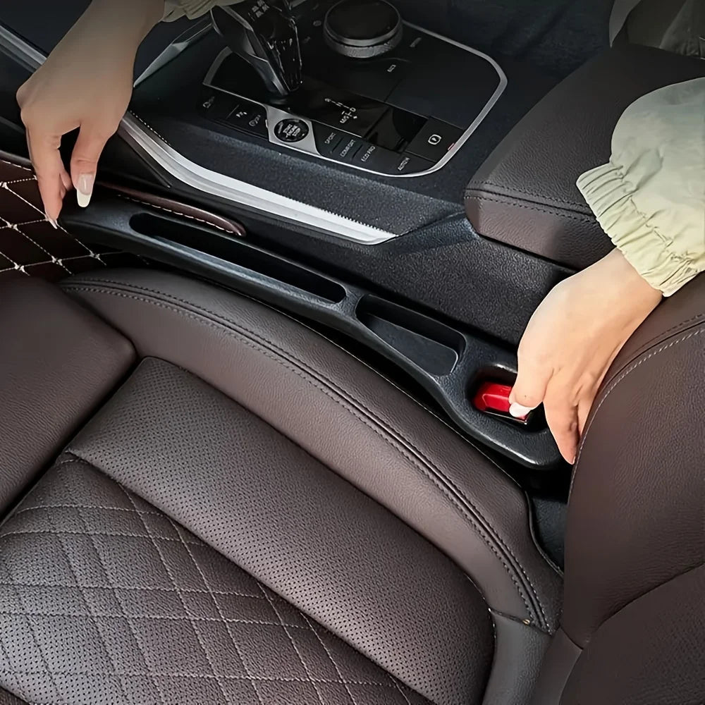 Two hands fitting a black strip into the seat-console gap beside a red seatbelt buckle