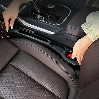 Two hands fitting a black strip into the seat-console gap beside a red seatbelt buckle