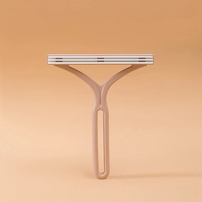 Tan plastic Y-shaped lint remover with fabric-covered comb head, studio shot on beige background