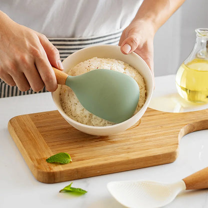 Hands using the sage green paddle to scoop rice into a bowl on a wood cutting board with mint leaves