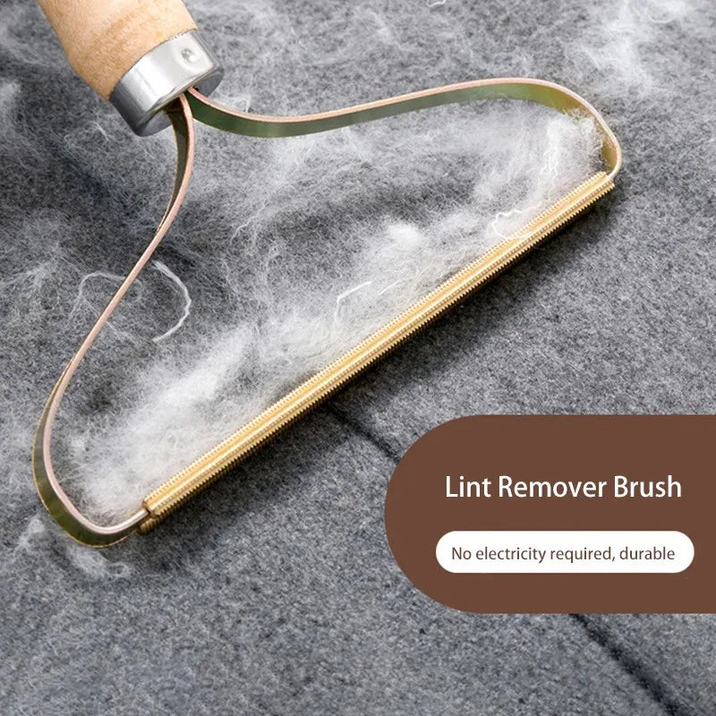 Angled shot of the comb with a thick clump of white lint caught in the gold teeth against grey fabric, labeled Lint Remover Brush