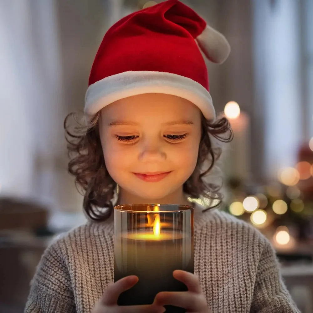 Child wearing a Santa hat holding a lit amber glass LED candle close to their face, smiling