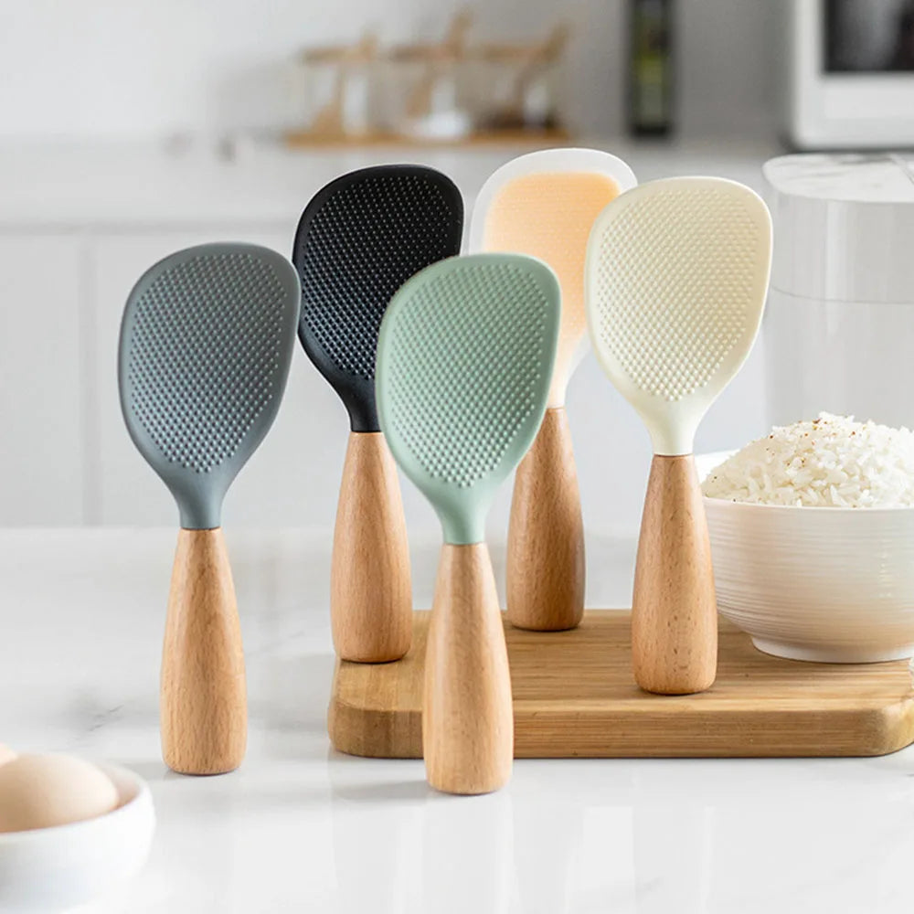 Five rice paddles in gray, black, beige, sage green, and white standing upright beside a bowl of rice