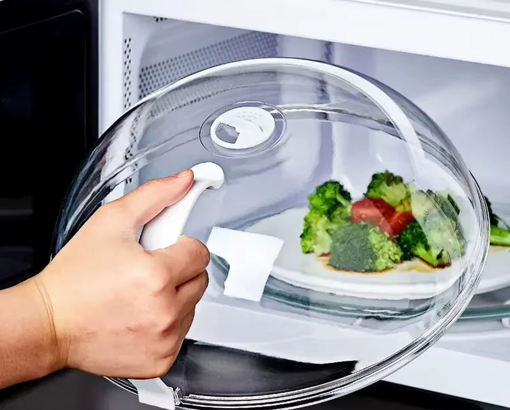 Hand lifting the clear microwave splash guard off a plate of broccoli and cherry tomato inside a microwave