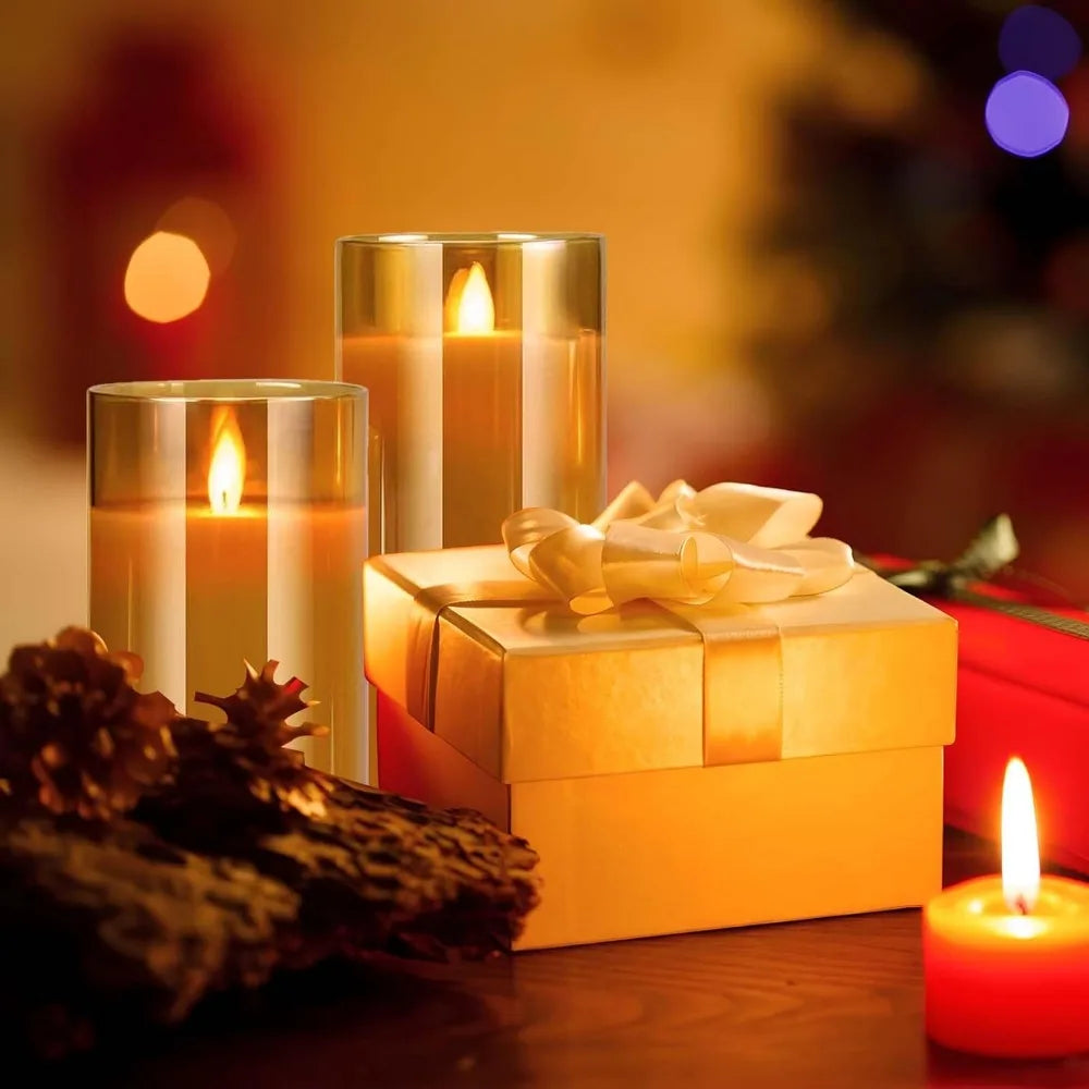 Two amber glass LED candles beside a wrapped gold gift box and a red candle, warm bokeh Christmas background