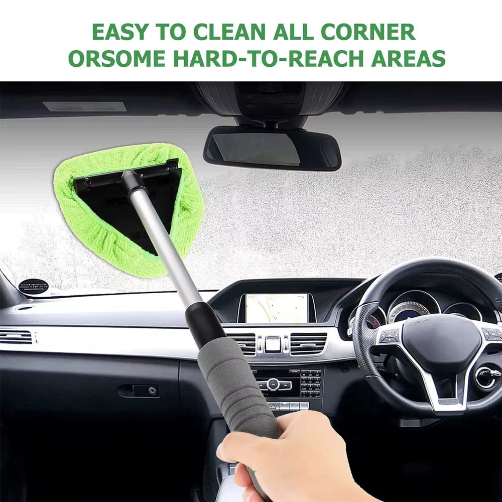 Green microfiber brush pressed against windshield from inside the car, hand gripping the handle