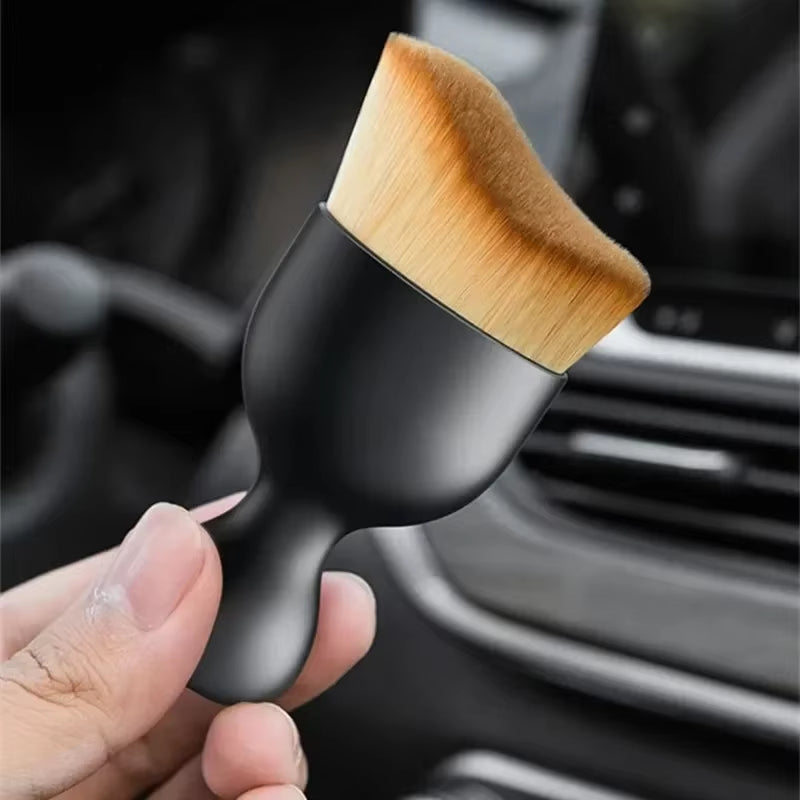 Hand holding the brush up near a car air vent with a blurred dashboard behind it
