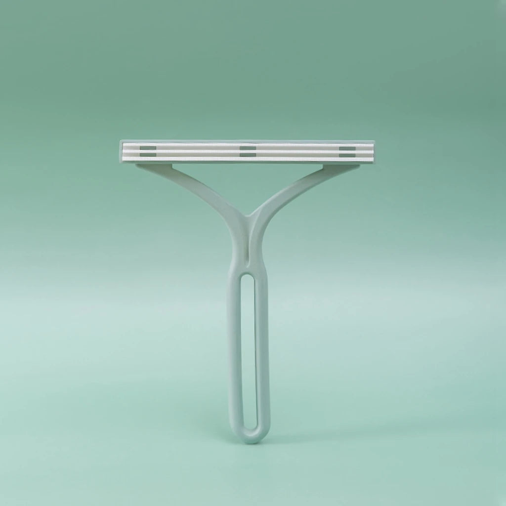 Sage-green plastic Y-shaped lint remover with fabric-covered comb head, studio shot on green background