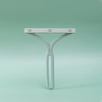 Sage-green plastic Y-shaped lint remover with fabric-covered comb head, studio shot on green background
