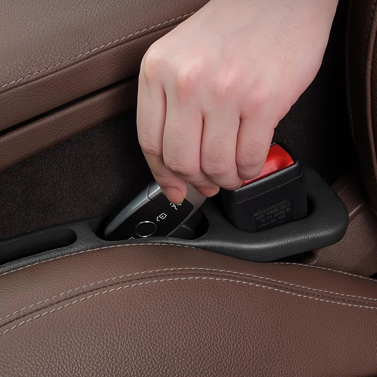Close-up of a hand pressing a key fob into the black gap-filler tray next to the seatbelt buckle