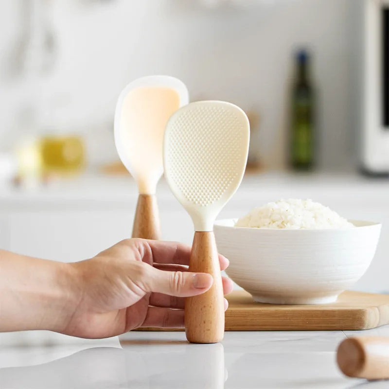 Cream and white rice paddles standing upright with a hand reaching for one beside a bowl of rice