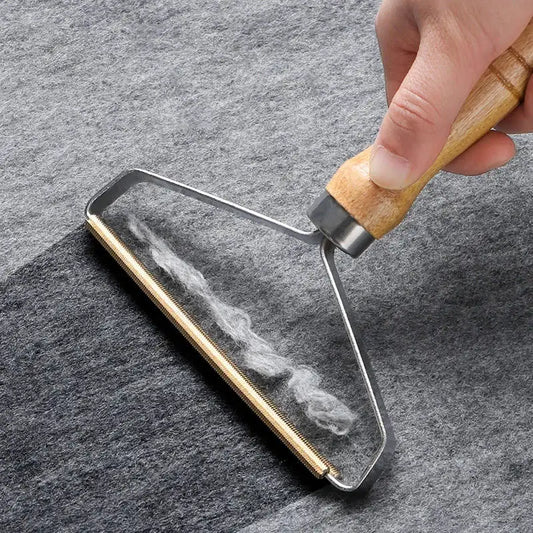 Hand holding the wooden-handled comb, gold teeth collecting grey lint fuzz off a grey wool fabric, close-up