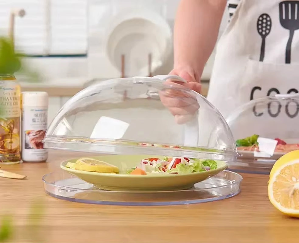 Hand lifting the dome cover off a green plate of salad, person wearing a kitchen-tool print apron