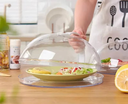 Hand lifting the dome cover off a green plate of salad, person wearing a kitchen-tool print apron